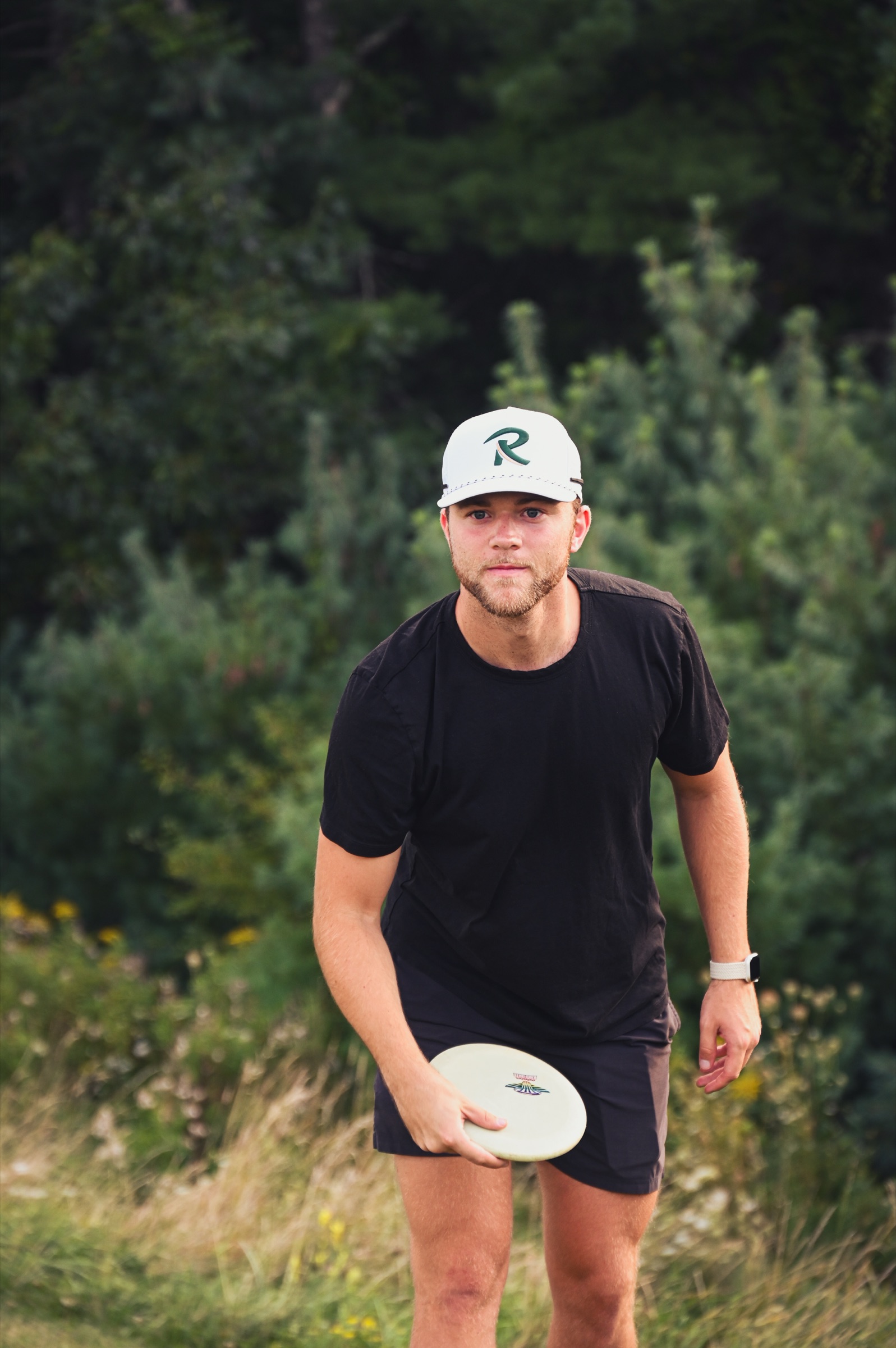 A player in a Radius cap walking the fairway, disc in hand, locked in